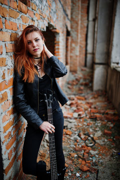 Red haired punk girl wear on black with bass guitar at abadoned place. Portrait of gothic woman musician.