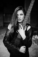 Red haired punk girl wear on black with bass guitar at abadoned place. Portrait of gothic woman musician.
