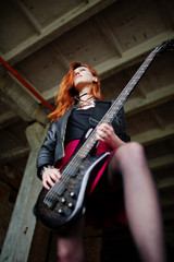 Fototapeta na wymiar Red haired punk girl wear on black and red skirt, with bass guitar at abadoned place. Portrait of gothic woman musician.