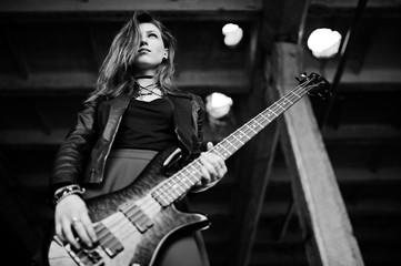 Red haired punk girl wear on black and red skirt, with bass guitar at abadoned place. Portrait of gothic woman musician.