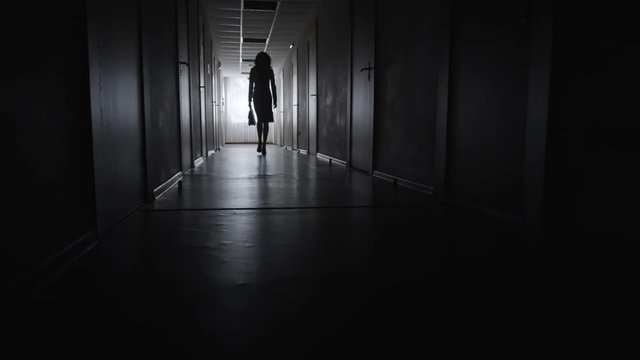 PAN of silhouette of unrecognizable businesswoman with briefcase walking along dark corridor of business centre 