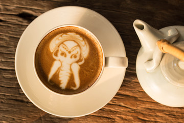 Ancient elephant design of Latte art coffee on wood table and part of tea pot beside , soft focus