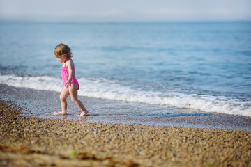 Fototapeta na wymiar The little girl runs on the beach at the seashore