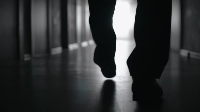 Tracking with low-section of silhouette of legs of businessman walking along corridor in slow motion