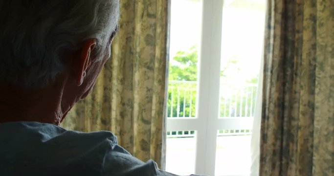 Senior man sitting in wheelchair looking through window in bedroom