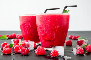 Raspberry cold refreshing cocktail and ice cubes on dark table