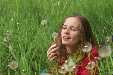 Portrait of the attractive woman in the grass considering a dandelion flower
