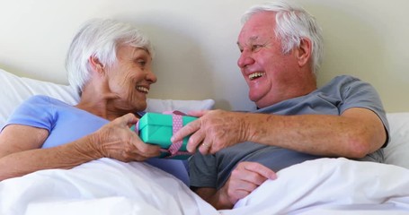 Senior man giving surprise gift to woman on bed in bedroom - Powered by Adobe