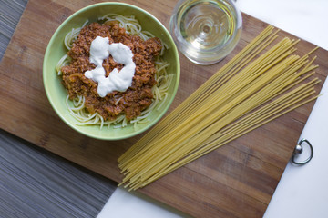 A bowl of spaghetti bolognese with some sour-cream and a glass of white wine