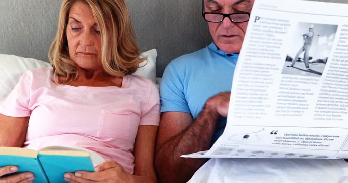 Senior couple on bed reading newspaper and book