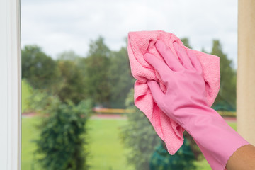 Hand in pink protective glove washing and cleaning window glass with microfiber cloth. Maid cleans window.