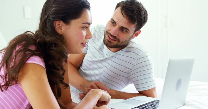 Couple interacting with each other while using laptop on bed