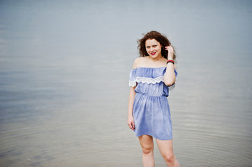 Portrait of a beautiful girl with curly hair wearing marine blye dress stands in the water.