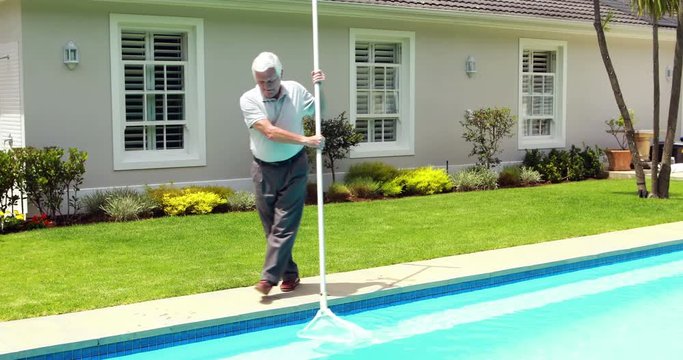 Senior man cleaning swimming pool with net