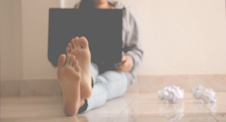 Woman sitting floor using laptop and crumpled paper.