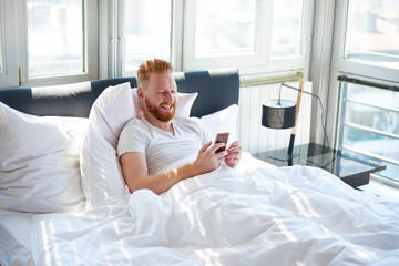 Young man texting messages over mobile phone while lying in bed