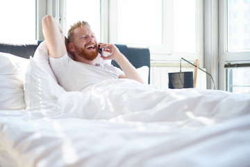 Young man talking over mobile phone while lying in bed