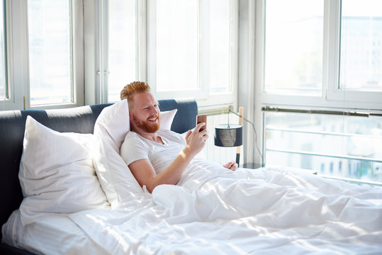 Young man texting messages over mobile phone while lying in bed