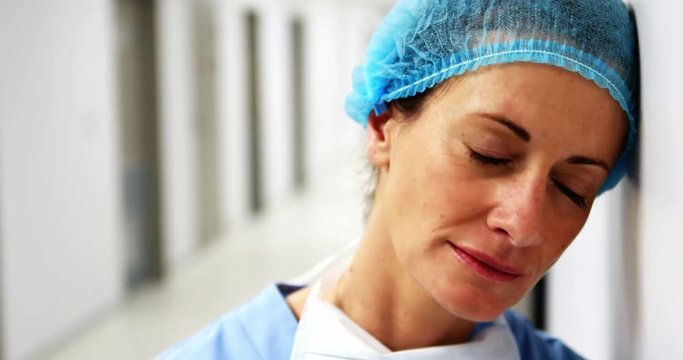 Sad surgeon leaning on wall in corridor