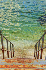 Rusty iron stairs descending into sea. Vertical orientation