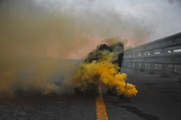 A brutal guy in a sweatshirt with colored smoke posing on the bridge magnificent advertising of colored smoke
