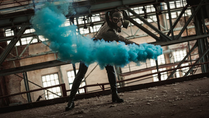 A girl in a gas mask and latex posing with colored smoke at a ruined factory magnificent...