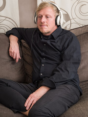 Mature man with white headphones on a couch.