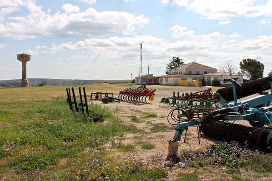 Farm tools with a water tower and a rural house in the background. Medinaceli, Spain. Summer 2014