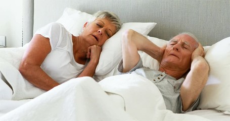 Senior man covering his ears while woman snoring in bedroom