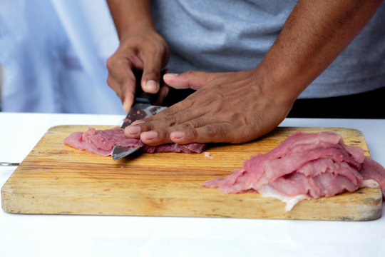 Chef cutting pork on a wooden chopping board with a very sharp knife.