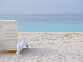 White plastic beach chair on a white sand beach with baby black-naped tern or sterna sumatrana on the right side.The bird belongs to Laridae family and lives in the tropical areas of the Indian Ocean