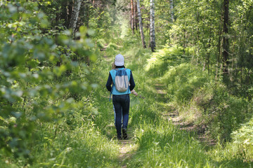 Teenager girl walking in forest at summer day, rear view