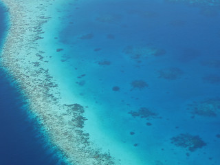Naklejka na ściany i meble Aerial view of an atoll in Maldives with underwater coral reef seen through clear blue sea water. Maldives is a tropical island country in Indian Ocean consisted of more than a thousand islands.
