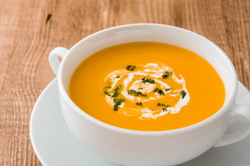 Pumpkin soup in white bowl on wooden table
