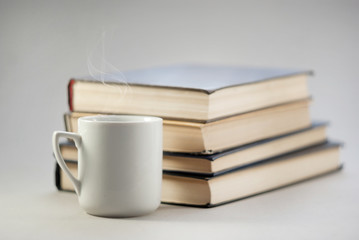 Vintage white cup with a hot drink on the background of a pile of books