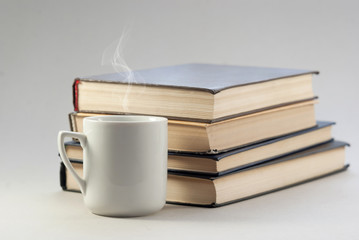 Vintage white cup with a hot drink on the background of a pile of books