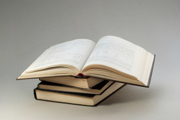 Old books with redened pages are stacked. Open book above