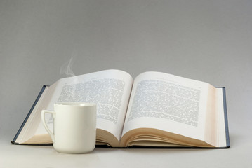 Fototapeta premium Vintage white cup with a hot drink on the background of an open book. Reading, background for postcards, poster, website. Clean composition.