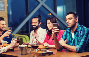 man with smartphone and friends at restaurant