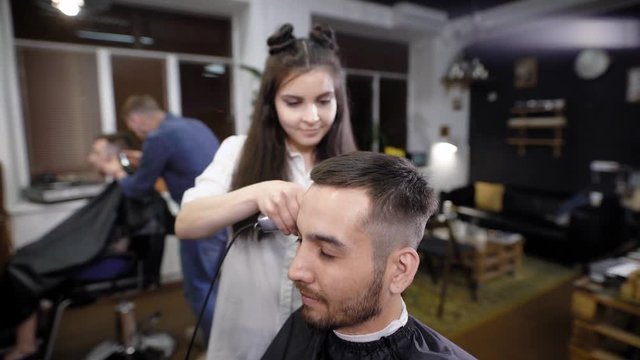 Woman barber trimming hair at her customer with hair clipper. Barber shop scene