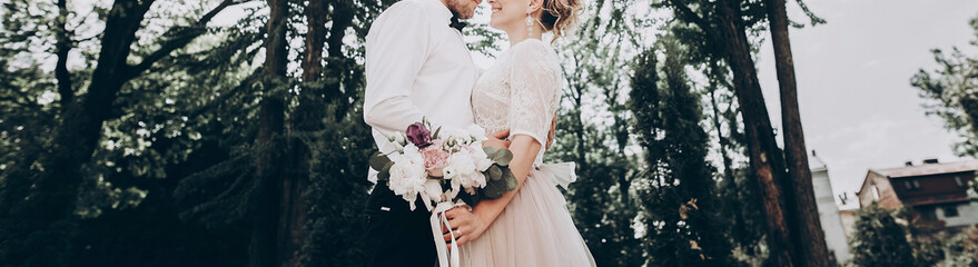 stylish wedding bride and groom hugging in sunny park, sensual moment. modern couple  embracing in garden in light. fine art wedding photo, romantic tender moment, long edge