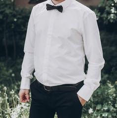 stylish groom in white shirt with black bow tie. wedding groom posing in sunny garden, fine art wedding photo, romantic moment