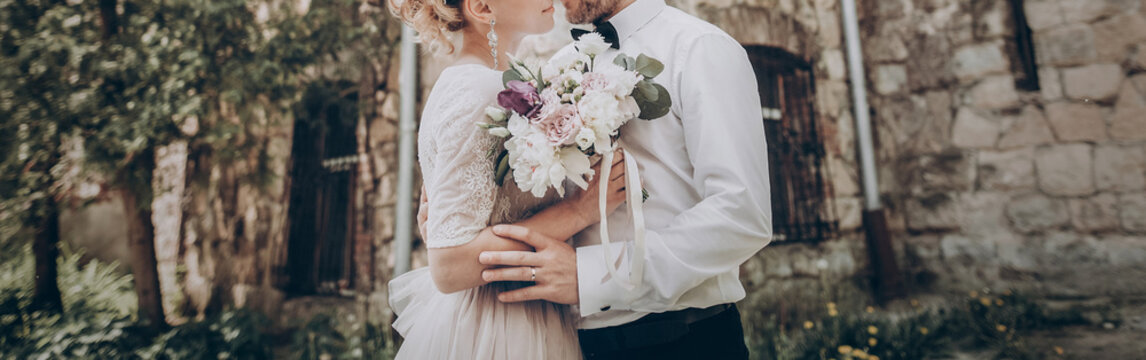 stylish wedding couple with bouquet. modern bride and groom holding fashionable bouquet at old  castle. fine art wedding photo, romantic moment, long edge