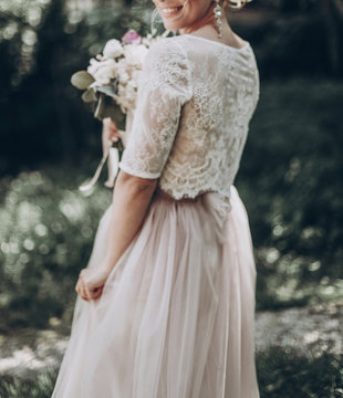 stylish wedding bride with bouquet and amazing modern dress. bride posing and smiling in sunny garden, dancing. fine art wedding photo, romantic moment, blurred defocused image