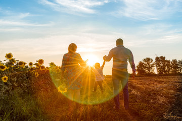 Happy family dad pregnant mom playing in the fresh air on the field near the sunflowers watching the beautiful emotional sunset in the backlight