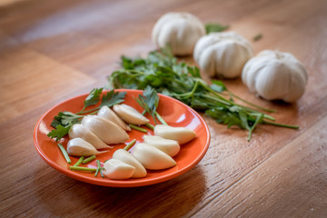 White garlic bulb in an orange plate and leaves of green parsley