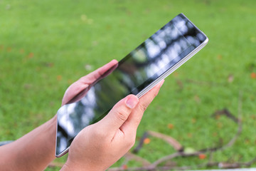 hand holding tablet in a park