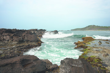 Fototapeta na wymiar Blue ocean waves crashing and splashing against brown rocks on the coast.