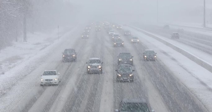Cars driving in traffic on a snow covered road during a winter blizzard