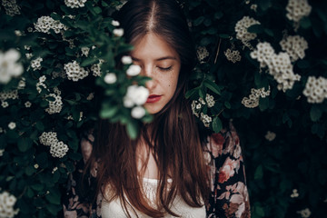 sensual calm portrait of beautiful hipster woman in blooming bush with white flowers of spirea....